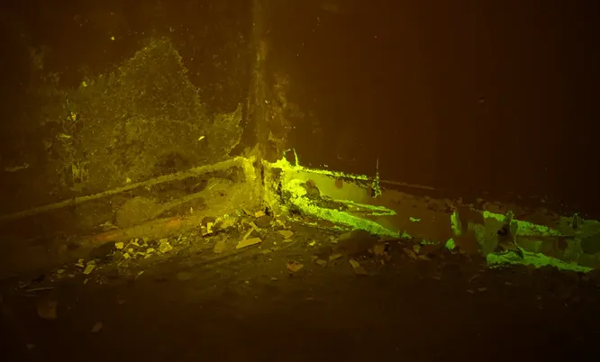 Bauforensische Untersuchung eines beschädigten Wand- und Bodenbereichs mit fluoreszierenden Spuren unter speziellem Untersuchungslicht.