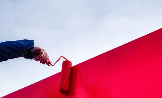 Handwerker trägt mit einer Farbrolle rote Farbe gleichmäßig auf eine Wandfläche auf, als Beispiel für professionelle Malerarbeiten.