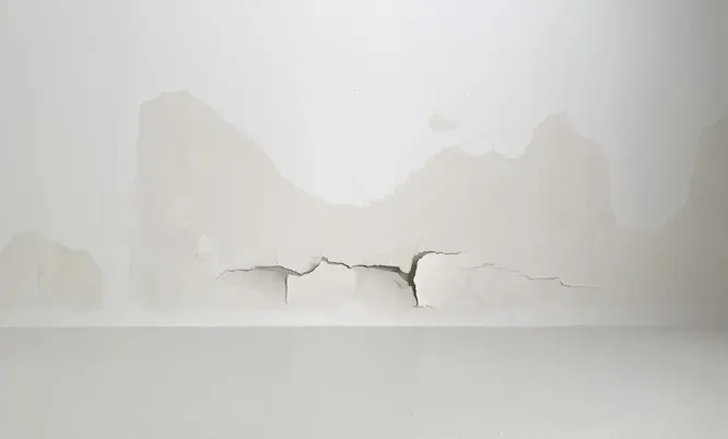 Wand mit großflächigen Feuchtigkeitsflecken und Rissbildung als Beispiel für einen zu begutachtenden Gebäudeschaden.